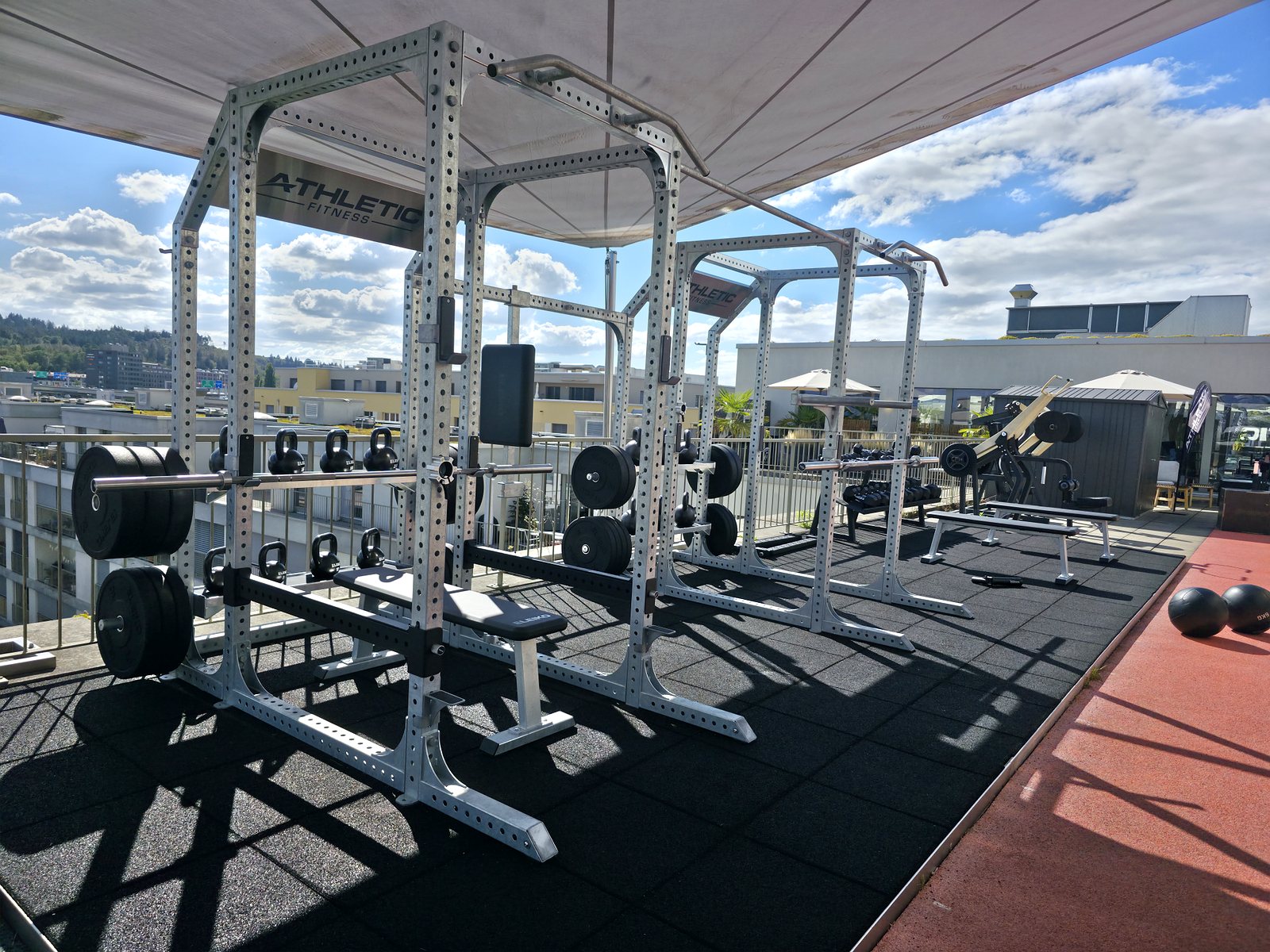 Espace de training extérieur sur un toit avec racks, bancs et kettlebells, réalisé par sc-fitnessprojects